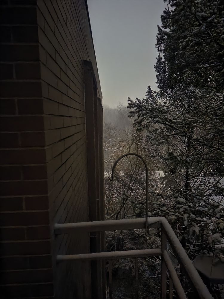 The side of a building during a snow storm. There's almost an inch on the ground 