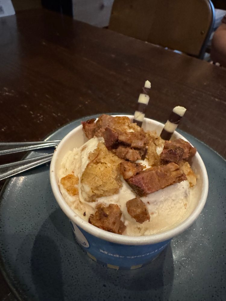 Paper cup of salted caramel ice cream with chopped up pieces of burnt ends on top.