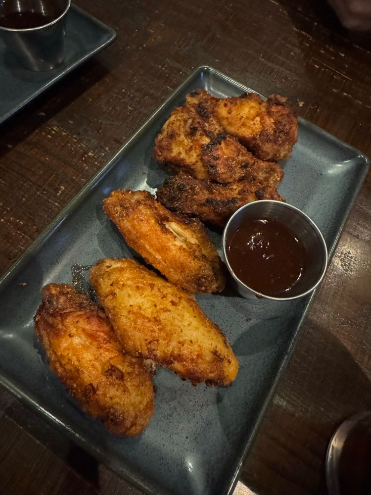 Dry runbed wings (6) on a rectangular plate with a metal sauce container with bbq sauce.