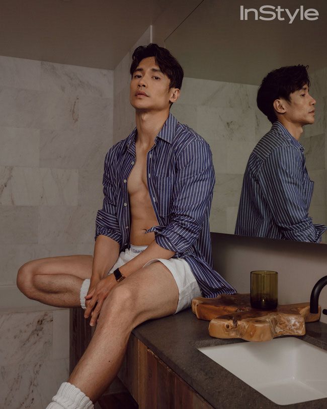 Manny in shorts and open shirt, sat down, smouldering