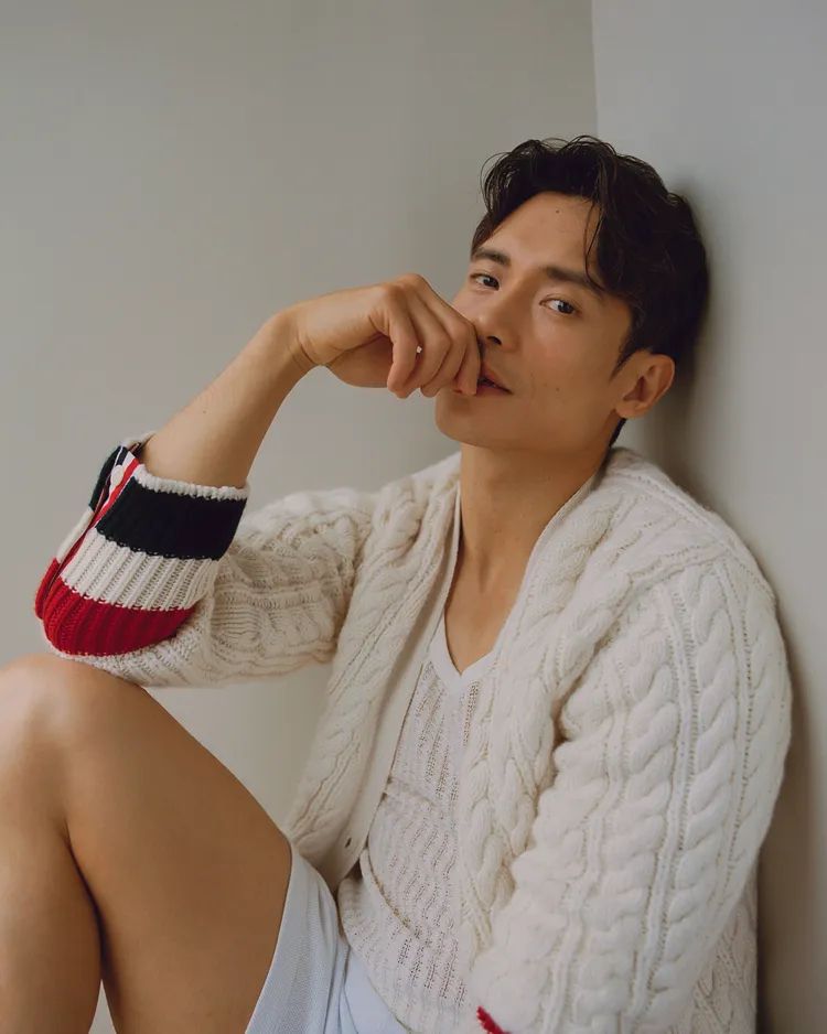 Manny in white knit cardigan and shorts, sat down, smouldering