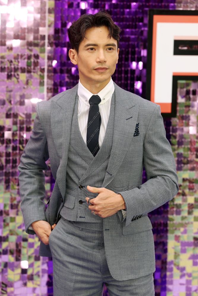 Manny in three piece grey suit, stood up, smouldering