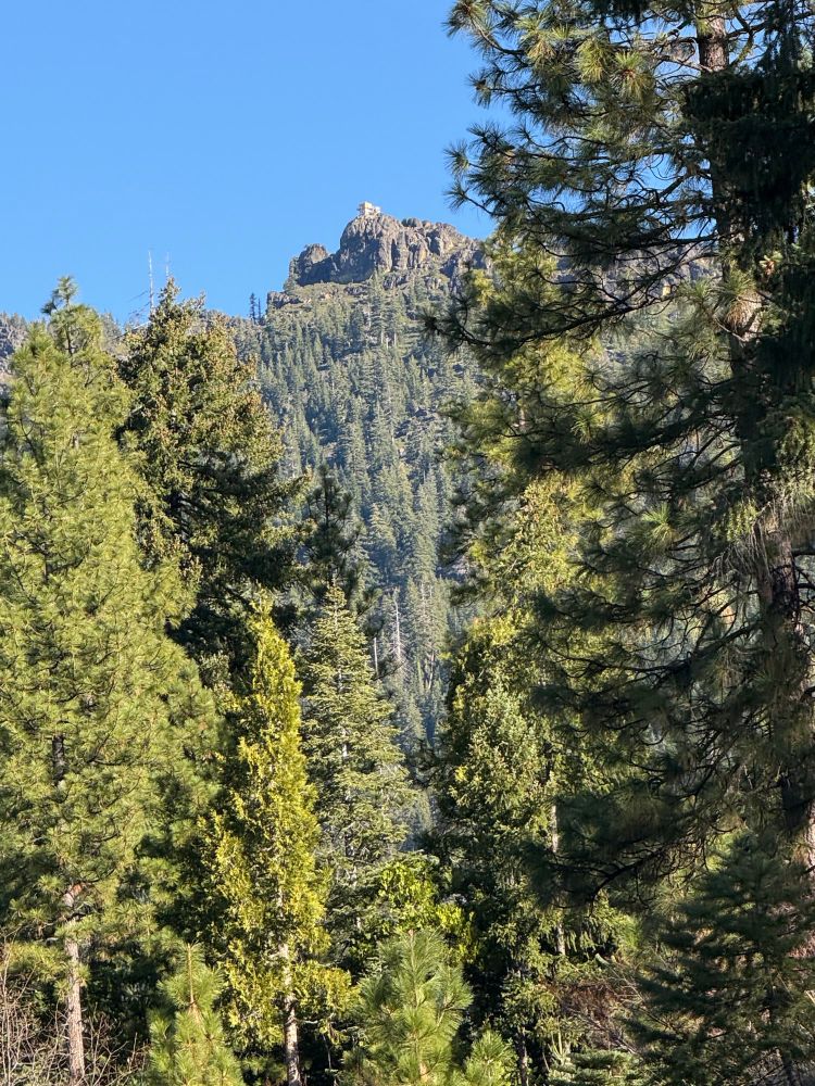 A fire outlook on top of a rock outcropping with evergreens on the mountainside 