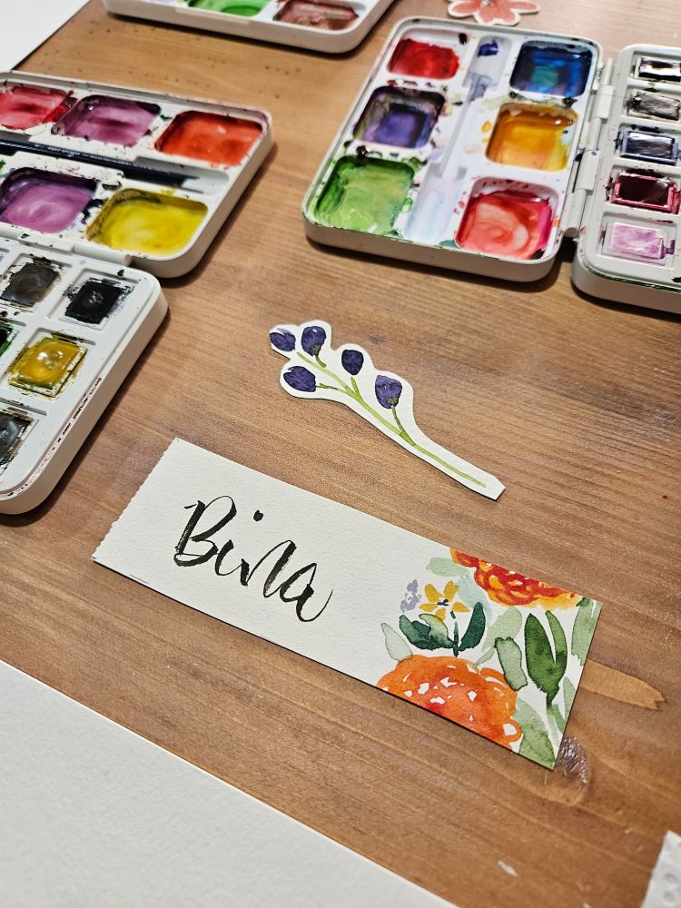 Ein gestaltete Namensschild, im Hintergrund mehrere Aquarellkästen.