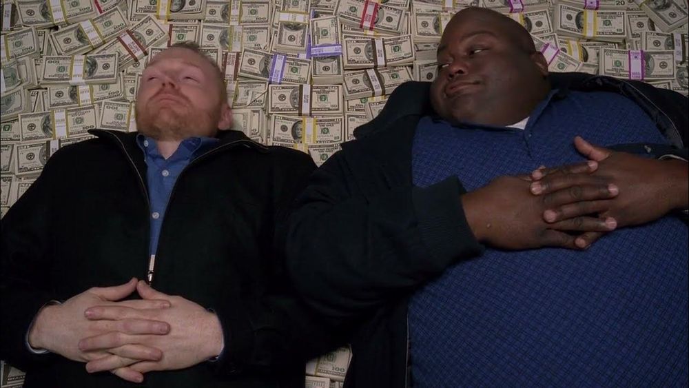 two gentlemen lie down on a massive stack of cash