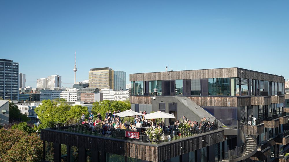 Eine gut gefüllte Dachterrasse. Im Hintergrund die Skyline Berlins mit Fernsehturm.