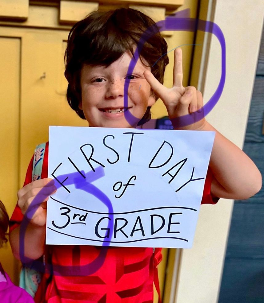 Kid holding a peace sign (two fingers) when his sign says 3rd grade
