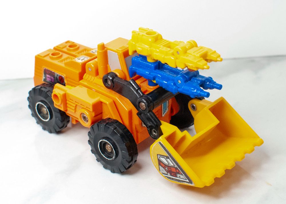 G1 Scoop, in altmode, with his Targetmaster partners, Holepunch and Tracer, equipped in gun mode in front of his cockpit.