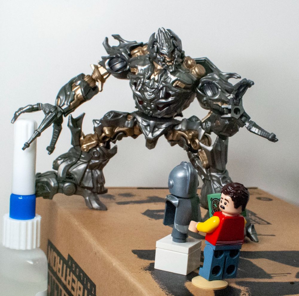 Blokees 2007 Megatron, looming over a custom Lego minifigure of Sam Witwicky with a cube (actually the cube from No Way Home). The whole scene's a recreation of their rooftop confrontation from Transformers 2007.