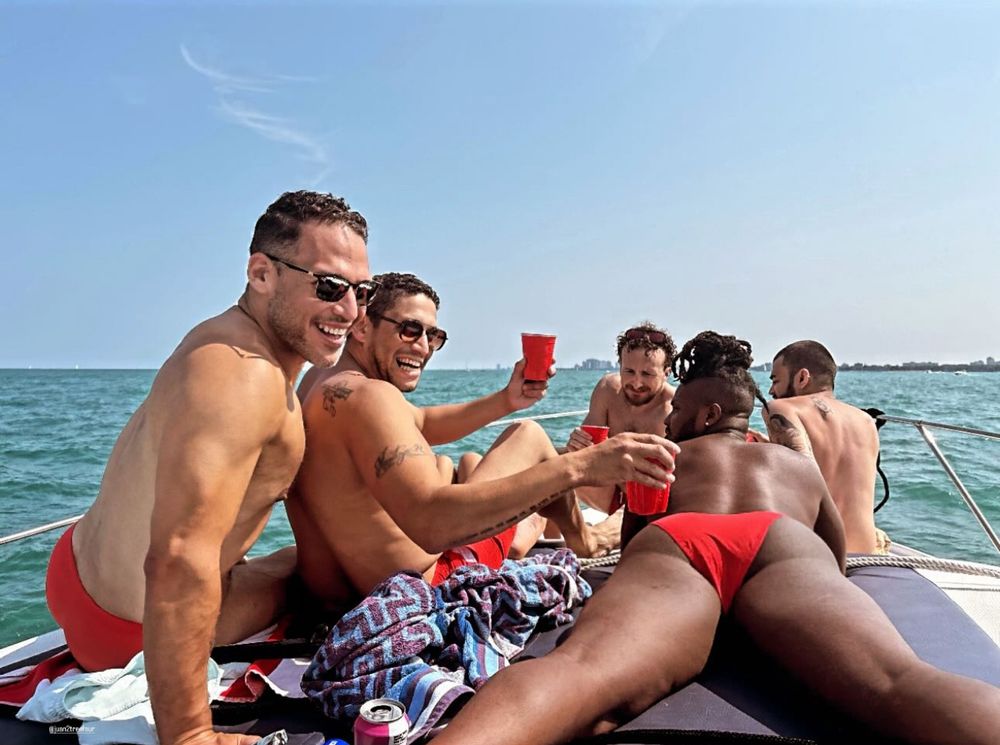 5 guys, sitting on a boat, turning back towards the camera, while out on the water.