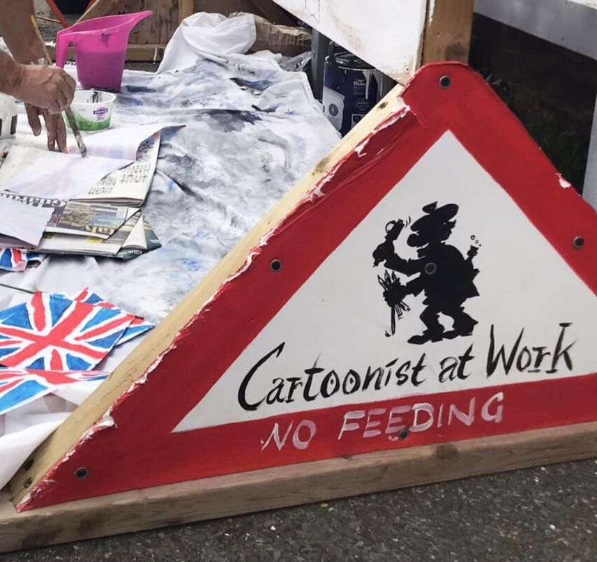 A picture of a cartoonist. A picture that encourages you, yes you, to get on a train, bus, car or donkey and make your way to Kent to support satire in challenging times and maybe even enjoy yourself. 