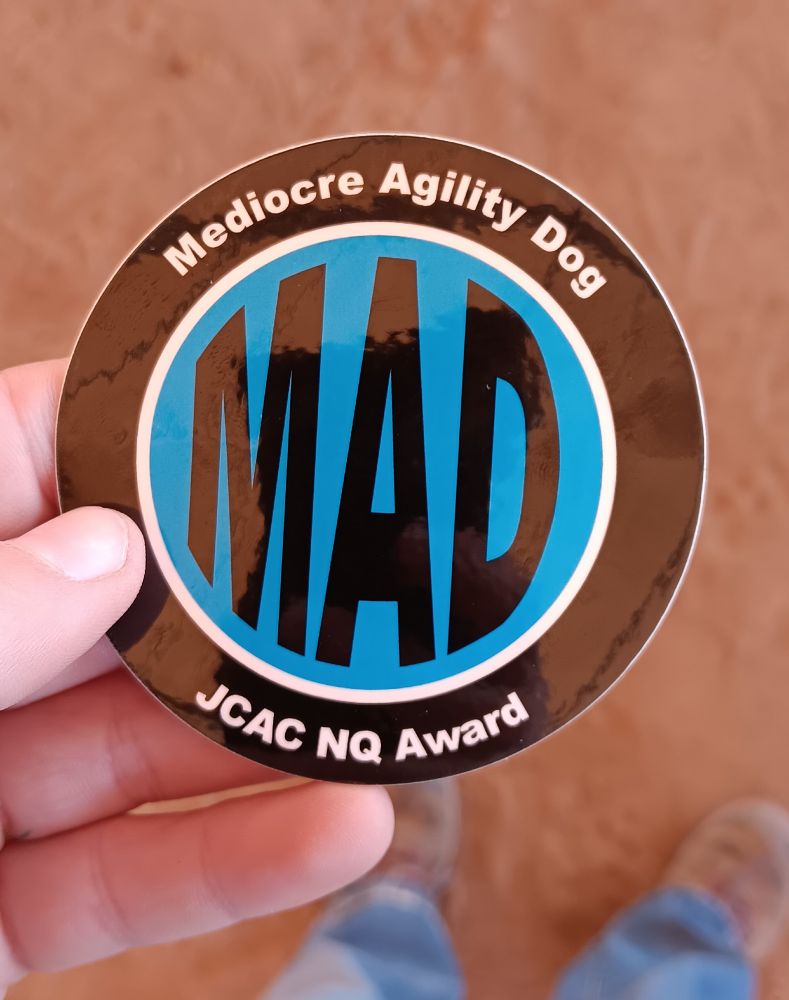 Round sticker with MAD written in the middle. Stands for mediocre agility dog. A non qualifying award. 