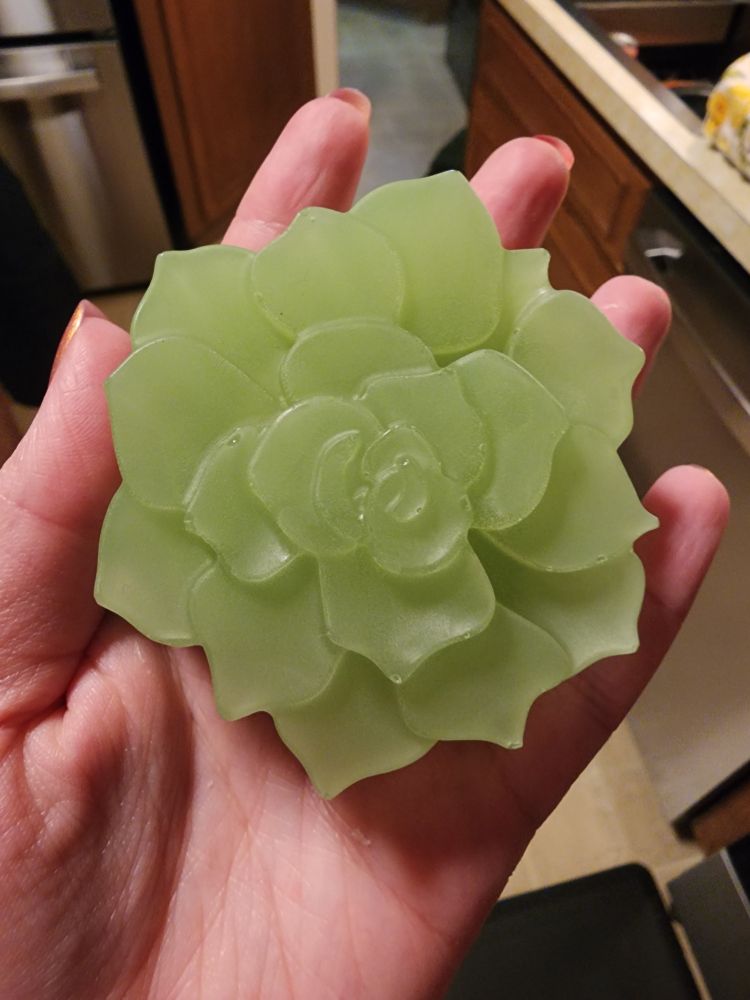 A hand holding a green soap bar in the shape of a succent or flower 