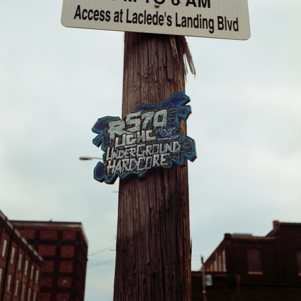 A photo of a handpainted particle board sign advertising a hardcore show from 2021 attached to a splintering wooden pole. Shot on Kodak Gold with a Minolta Autocord.