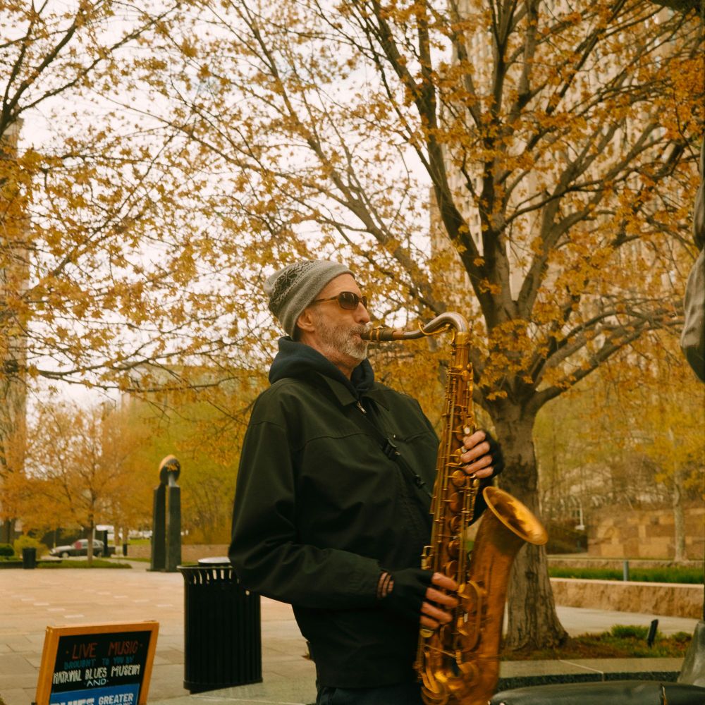 A man in a park playing saxophone. Shot on Kodak Gold with a Minolta Autocord.
