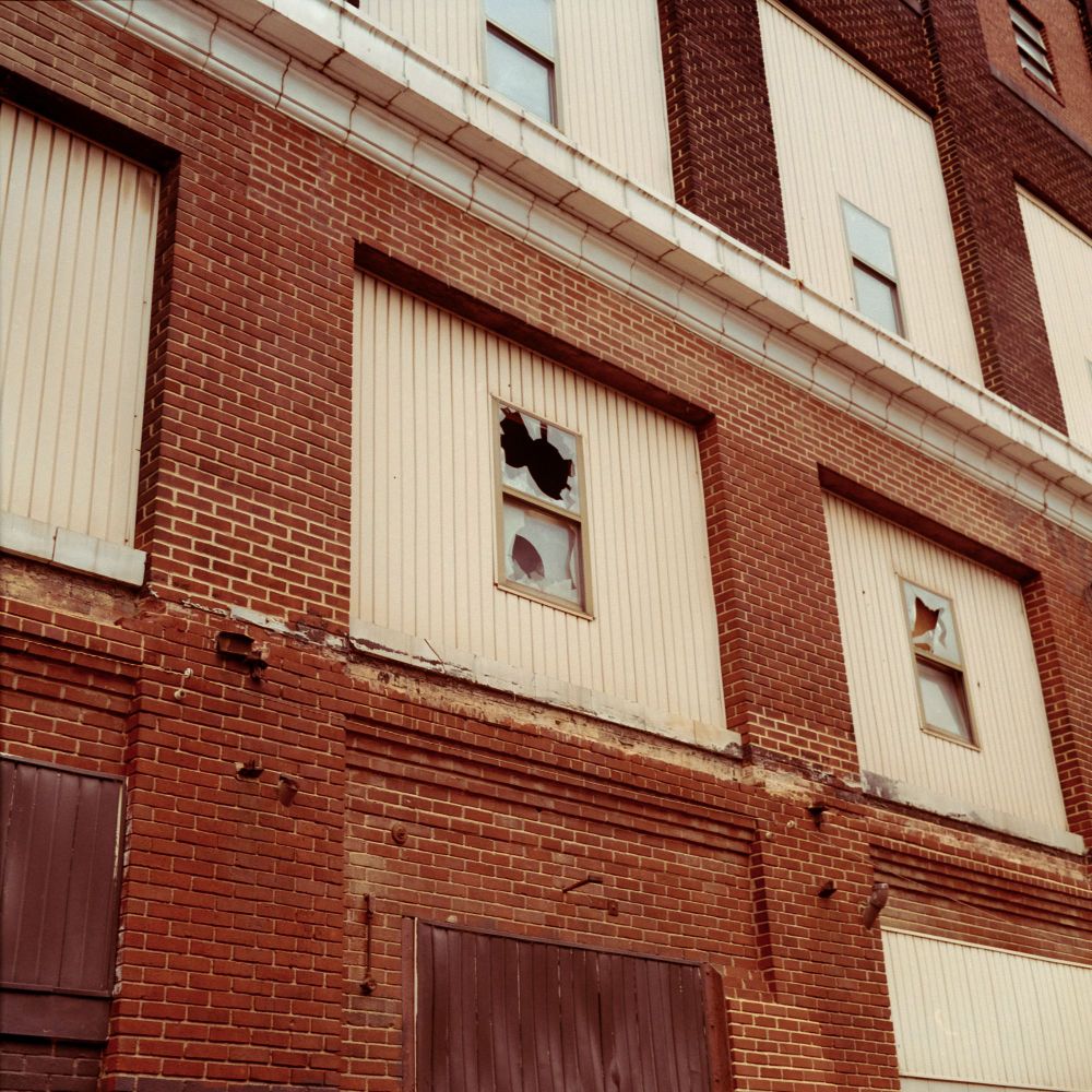 A brick warehouse building with some wooden? siding and broken windows. Shot on Kodak Gold with a Minolta Autocord.