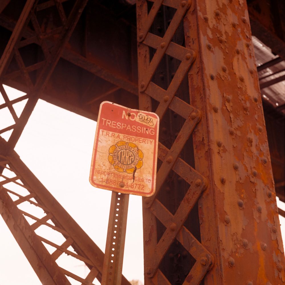 A photo of a tarnished "No Trespassing" sign against a rusting steel bridge. Shot on Kodak Gold with a Minolta Autocord.