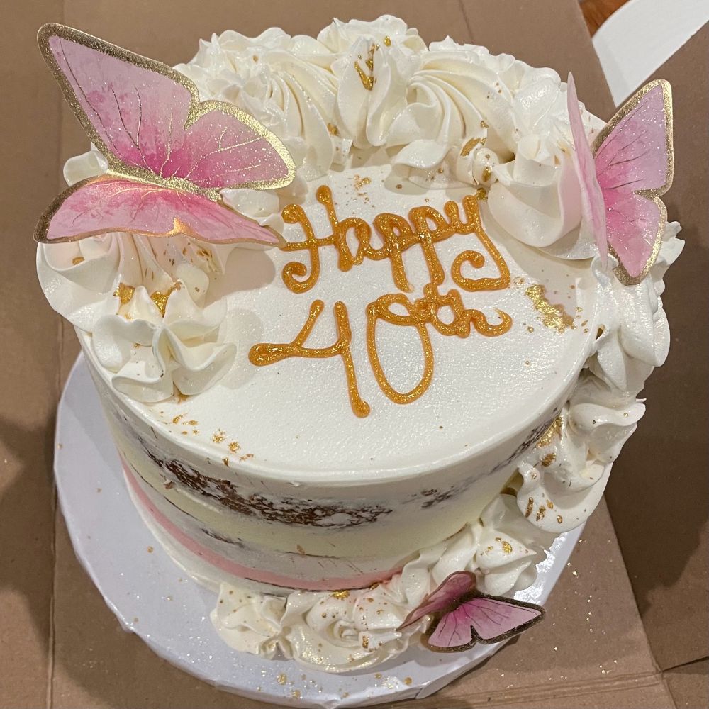 A cake that says Happy 40th. The cake is decorated with white buttercream rosettes, pink butterflies, and a dusting of edible gold powder. It was delicious.
