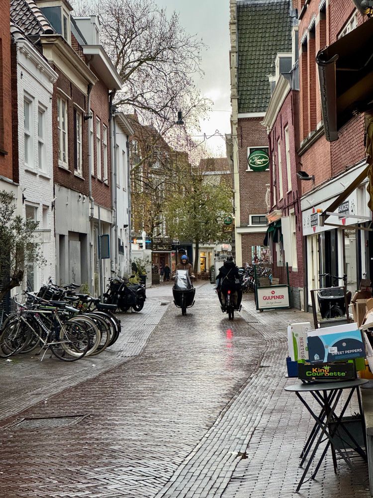 Two cargo bikes pass each other on wet cobblestone streets in the main center portion of the city