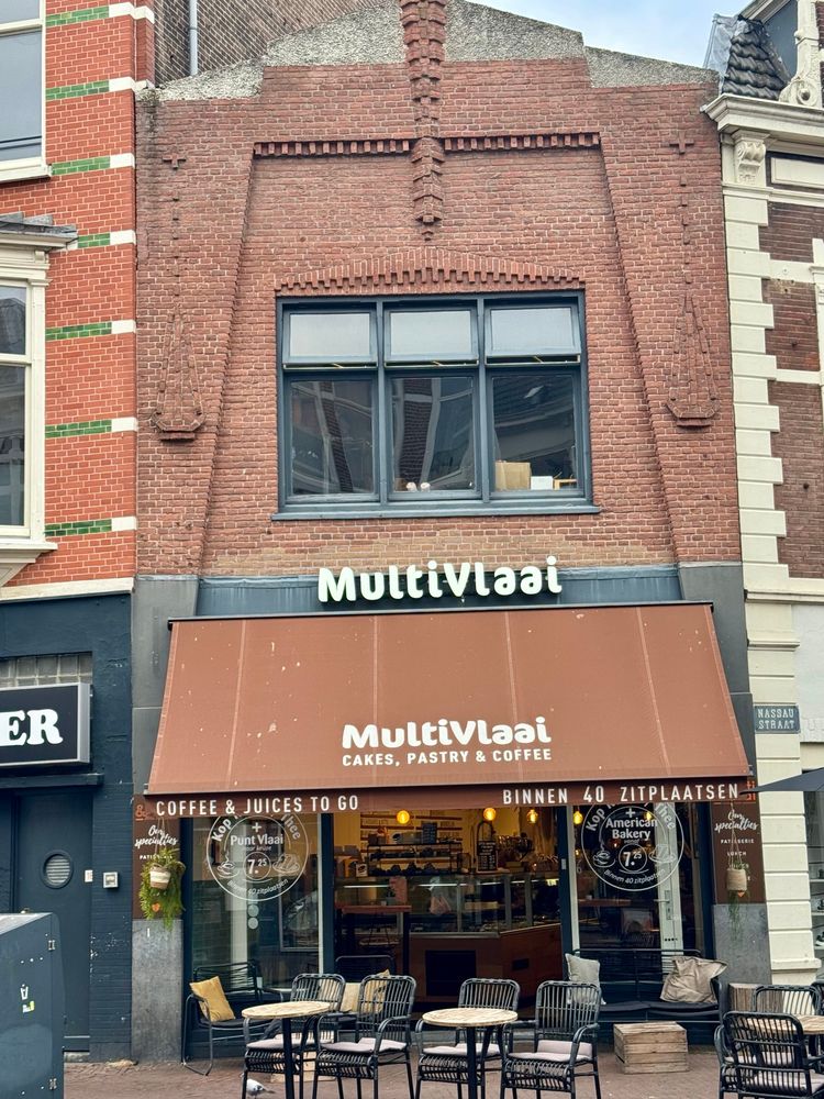 A brick art deco building at the corner of shallow turn along the main street. The tables are all out for the morning, but no one is sitting there yet.