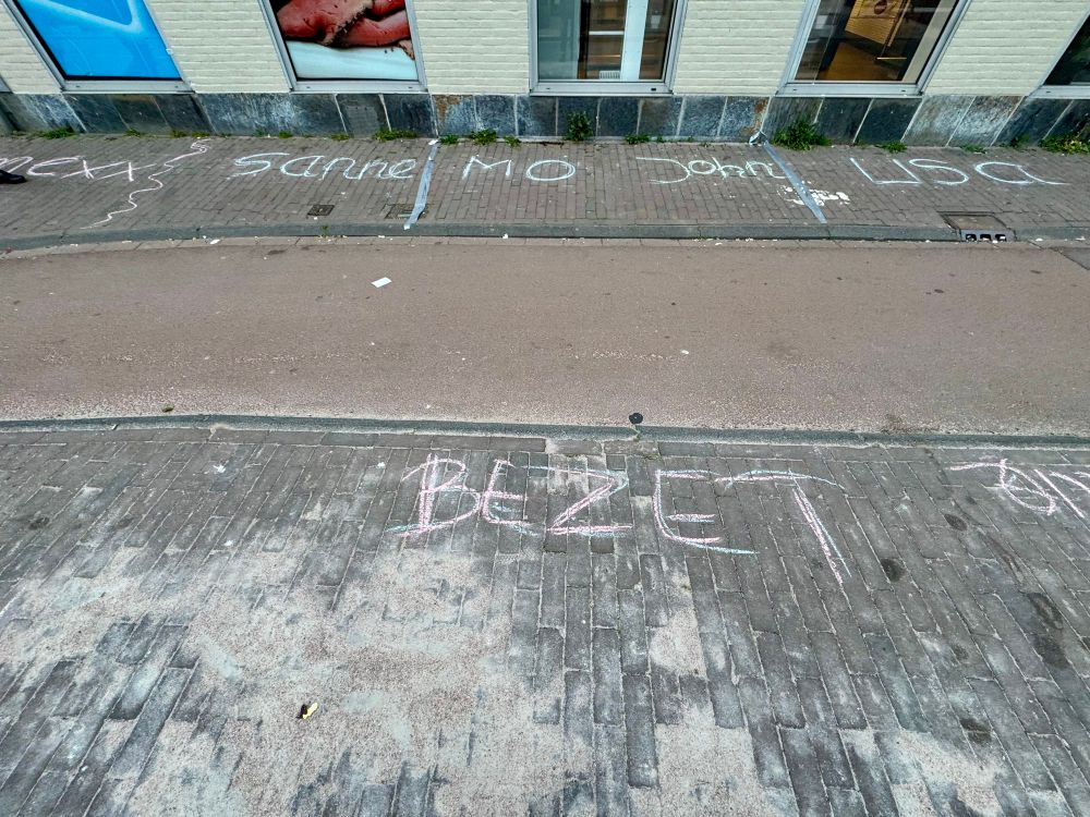 A sidewalk where children have written their names or written occupied in chalk, dividing up the areas where they will sell their stuff on King’s birthday