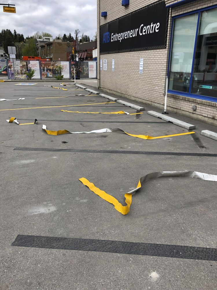 A parking lot with tape lines to mark the parking spaces, several of the tapes having come undone and warped