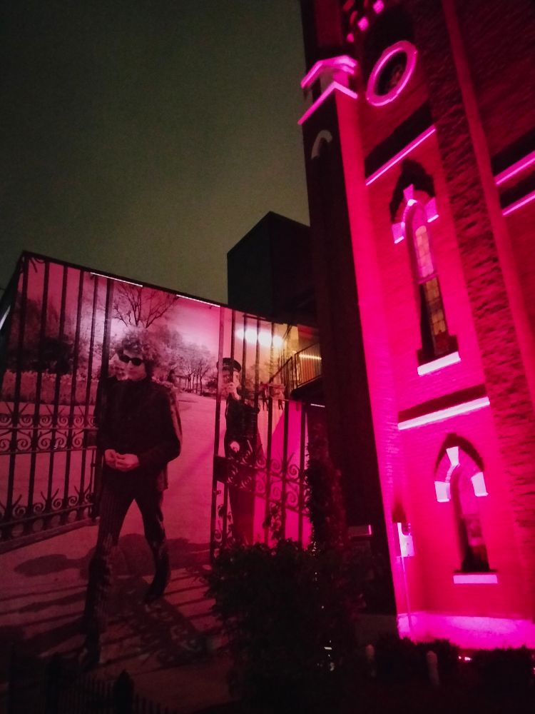 Outside of The Last Refuge with a pink wash light over Dylan's photo