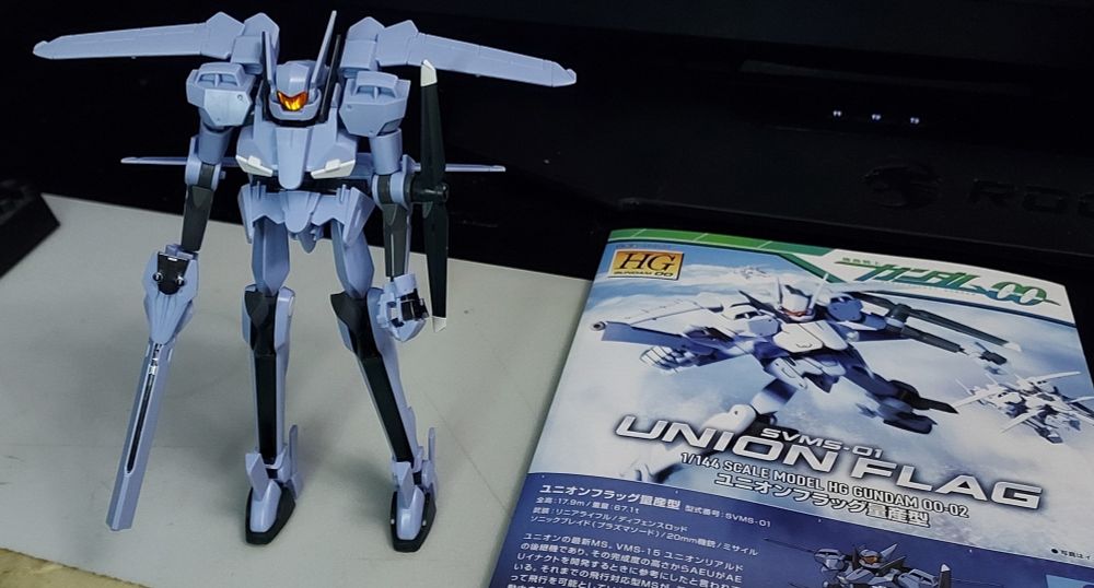 a picture of a completed gunpla kit posed next to the instruction manual