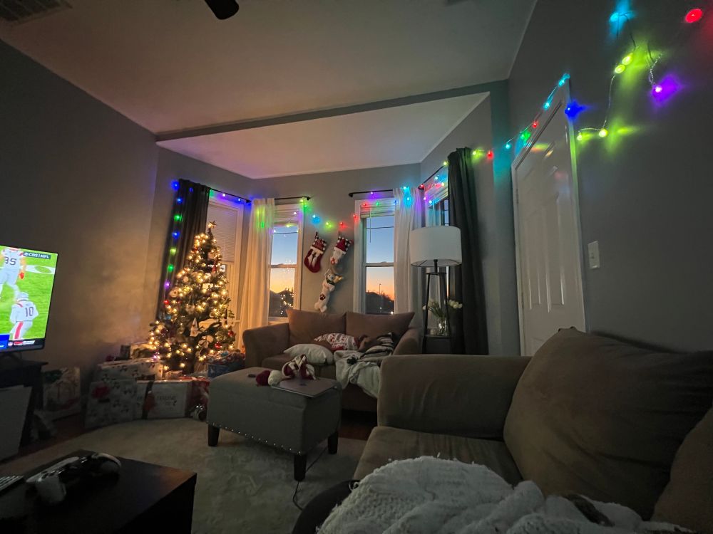 A living-room area with a Christmas tree, presents, and decorations. A sunset seen through the windows.