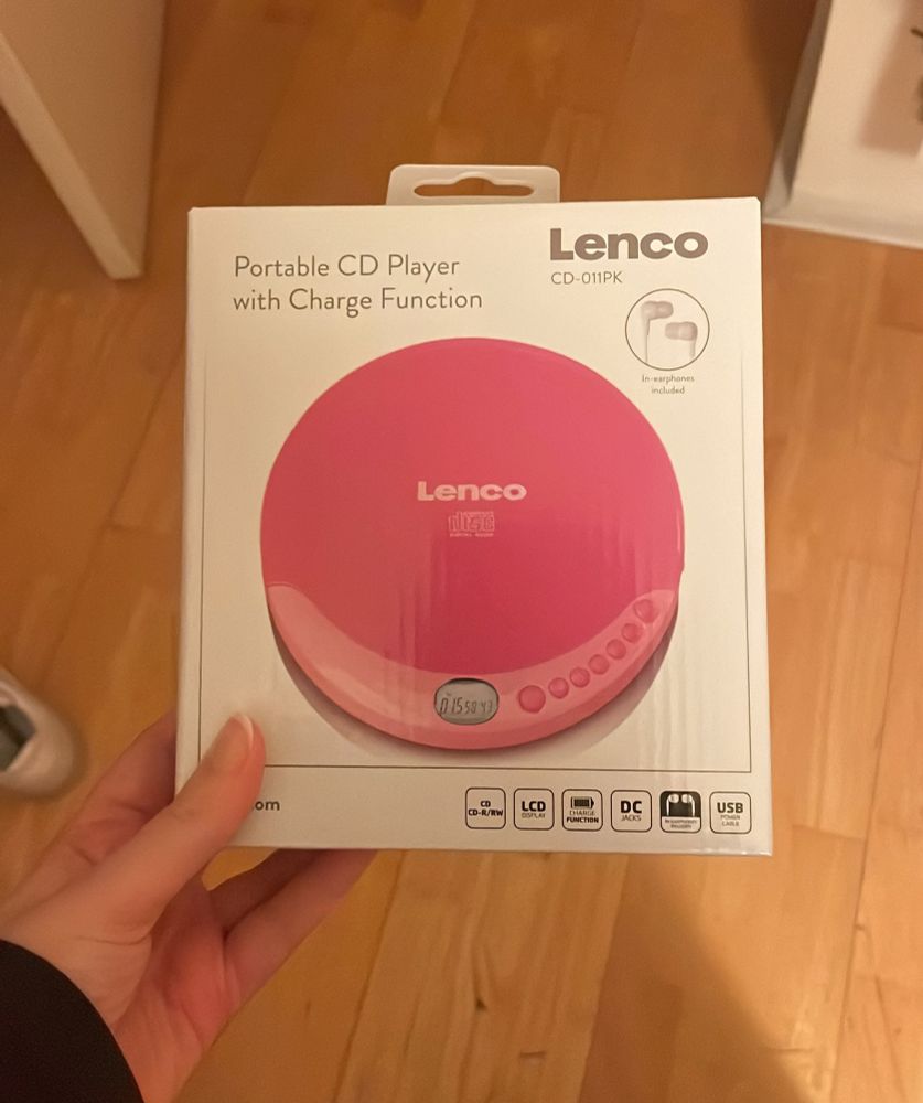 a photo of my hand holding the white packaging of lenco's pink portable cd player. 