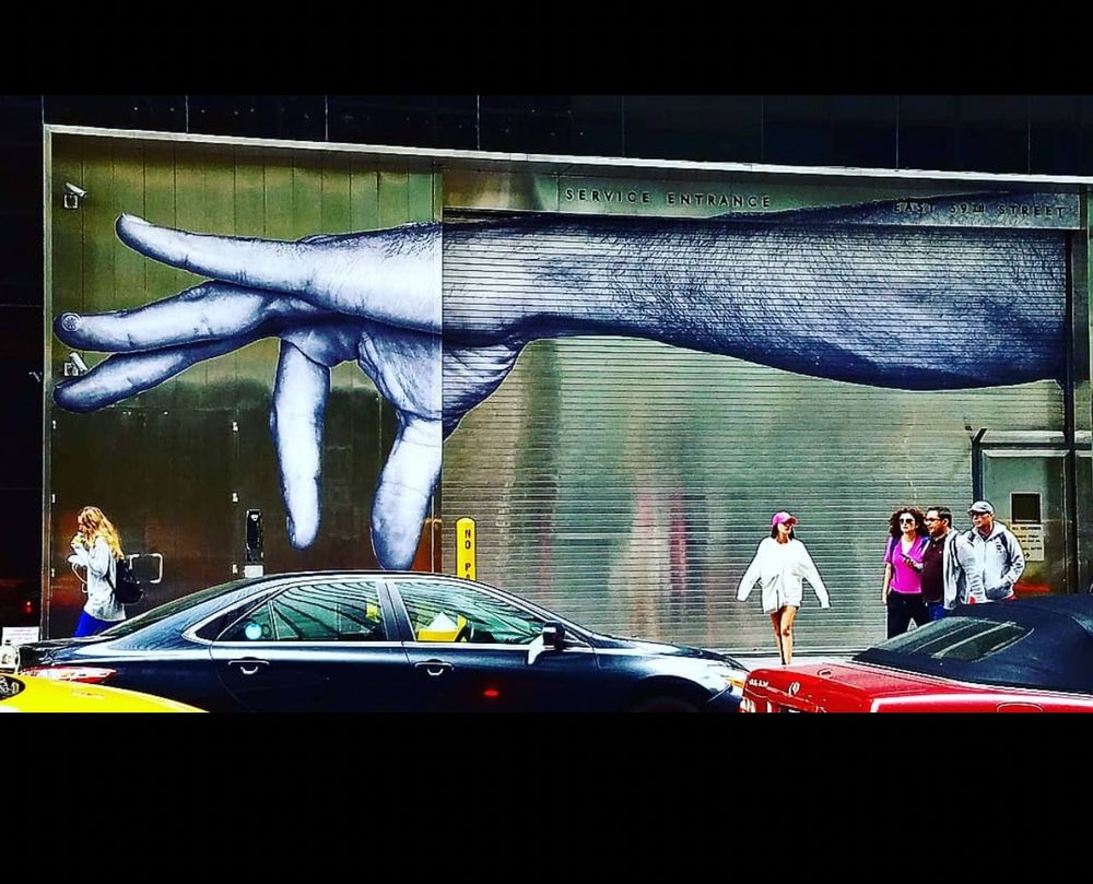 Grafitti on service entrance of garage. Large arm and hand, hand in position looking like it is plucking or pitching the car parked in front.