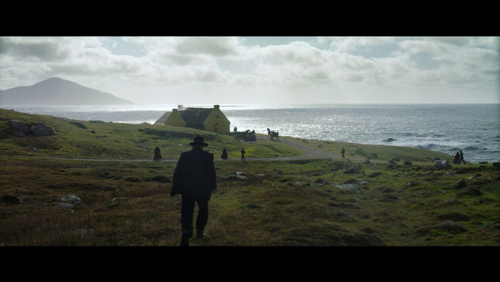 Villagers in dark colors amble across green toward a cluster of houses.