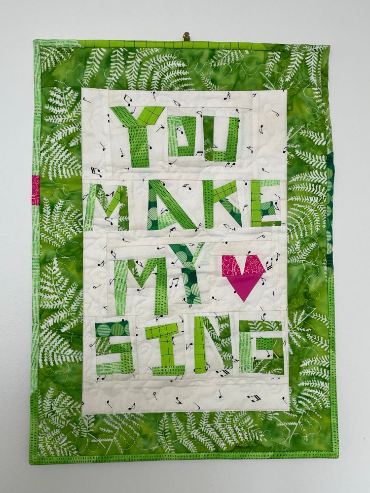 Small quilt with improv lettering that says “you make my heart sing” Heart is a pink improvised heart 