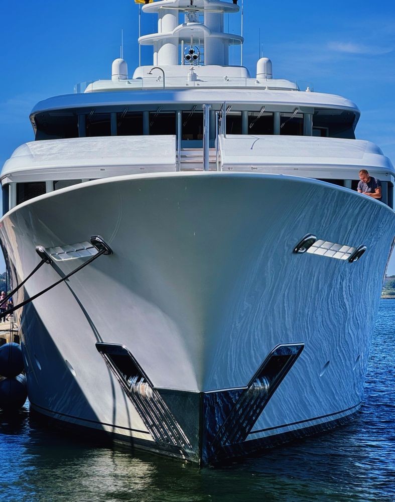 Das Foto zeigt eine Luxusyacht mit weißem Rumpf, modernem Design und mehreren Decks, im Hafen bei sonnigem Wetter vertäut.