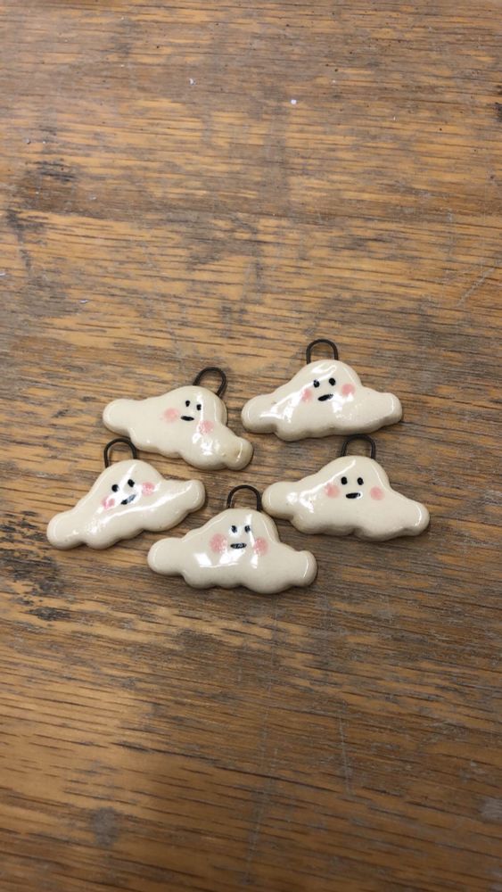 Image is of five small ceramic clouds with pink cheeks and little smirks grouped together on a worn wooden table top 