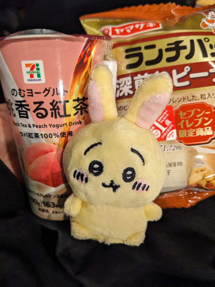 左にセブンイレブンの
「のむヨーグルト　桃香る紅茶」
中央にちいかわのうさぎの小さいぬいぐるみ
右にセブンイレブン限定の
「ランチパック　深煎りピーナッツ」