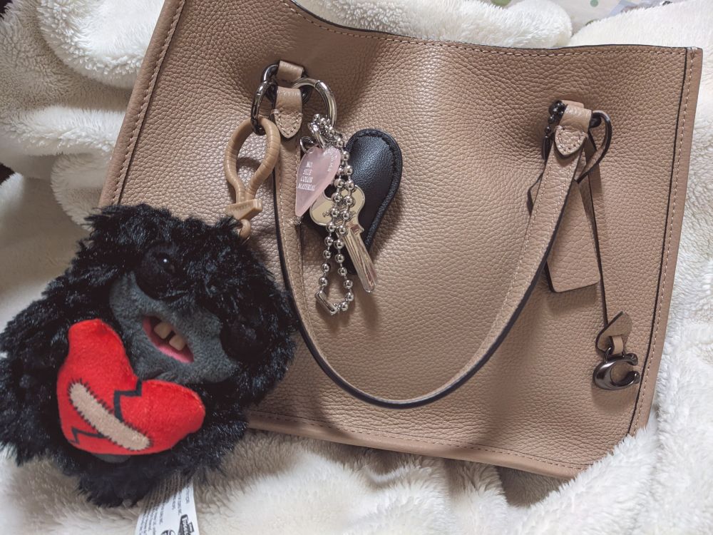 ベージュのコーチのバッグに、きのうお迎えした黒くて赤いハートを抱えているファグラーと、GOLDYのレザー調ハートチャーム（黒）が付いている。