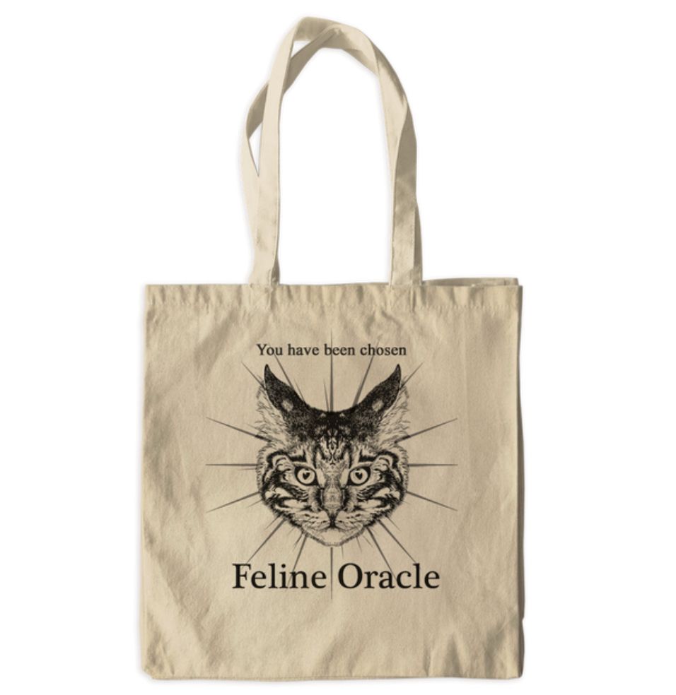 A tote bag with a drawing of a cat head. Above and below the drawing are the words “you have been chosen. Feline Oracle.”