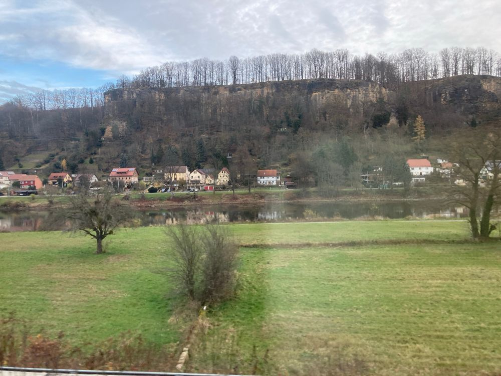 Fields in foreground and wooded bank on far side of river