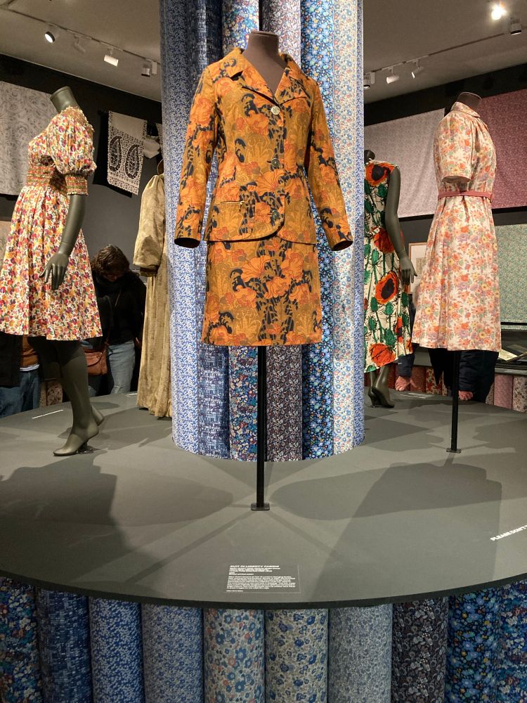 Suit displayed on stand with others around a central pillar made from fabric rolls.