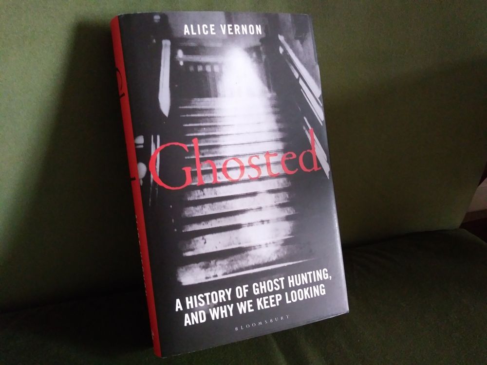 A hardback copy of Ghosted: A History of Ghost Hunting, and Why We Keep Looking by Alice Vernon. The cover features a ghostly image on a staircase in black and white, with the word 'Ghosted' in the middle in red font.