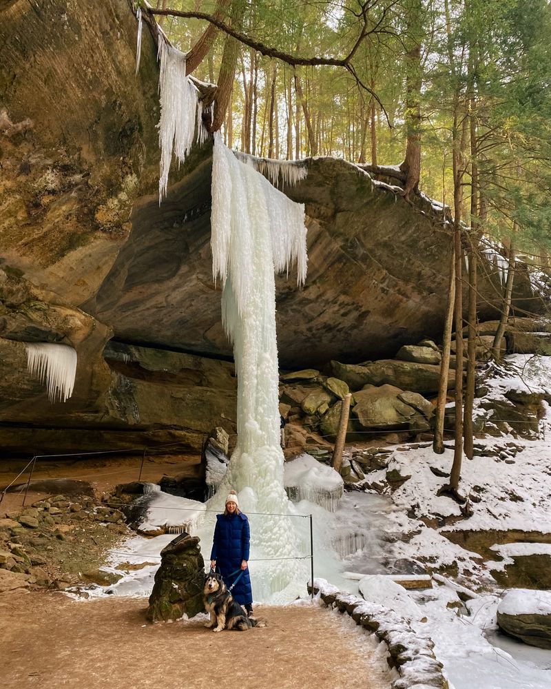 a woman and dog posing on a snowy hiking trail in front of large icicle