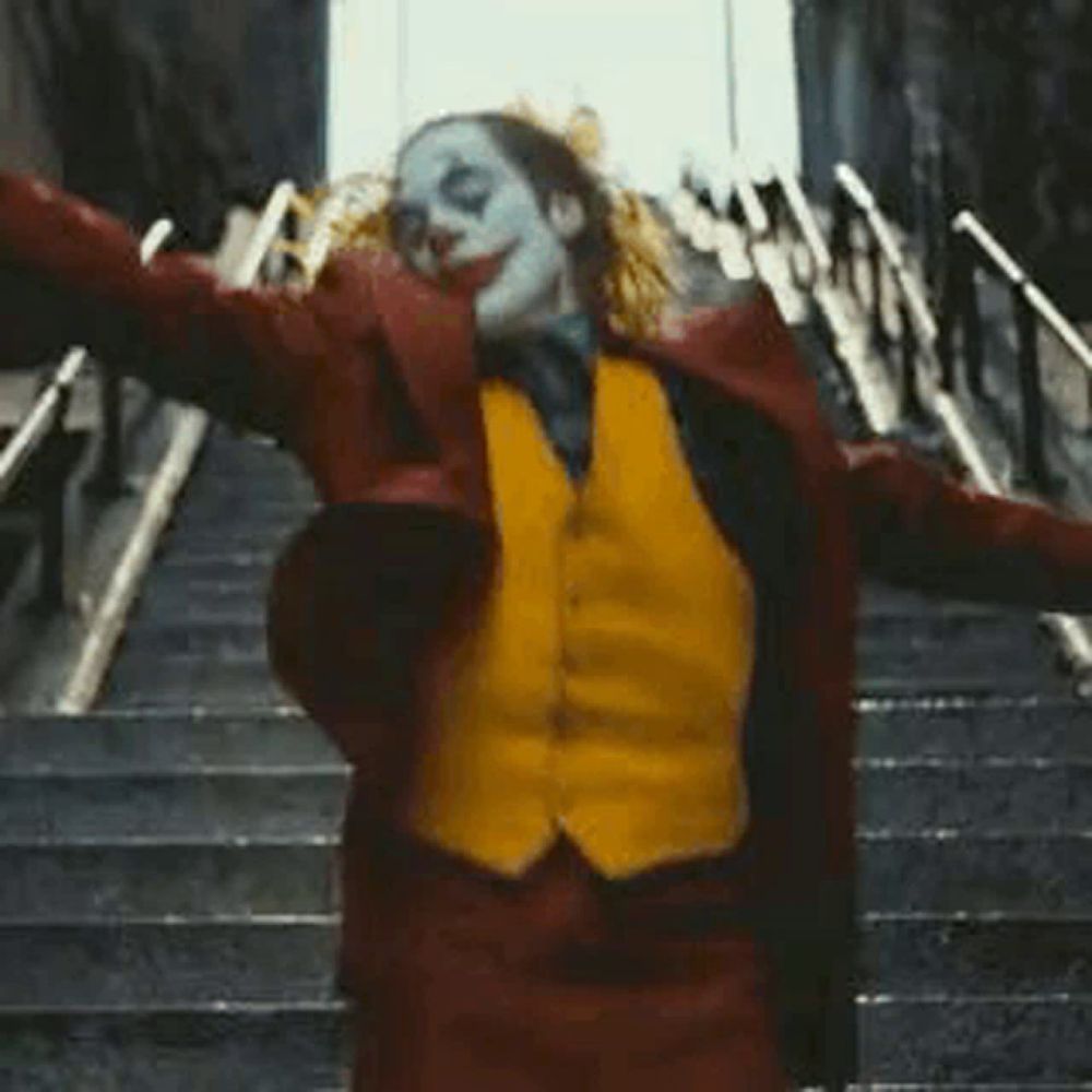 the joker is standing on a set of stairs with his arms outstretched and smiling .