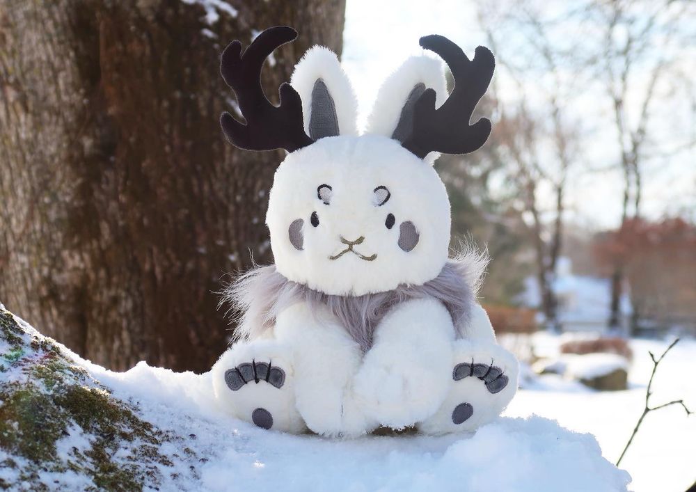 White Jackalope with grey furry mane and black antlers in the snow