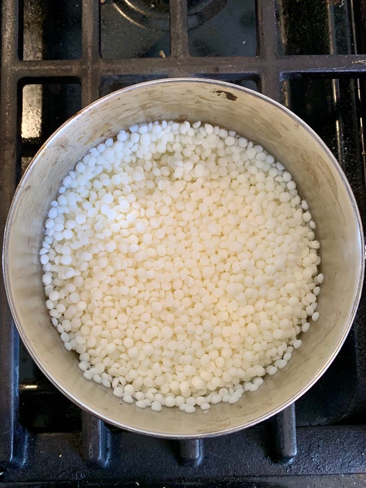 A pot of coconut wax pellets melting on a gas stove.