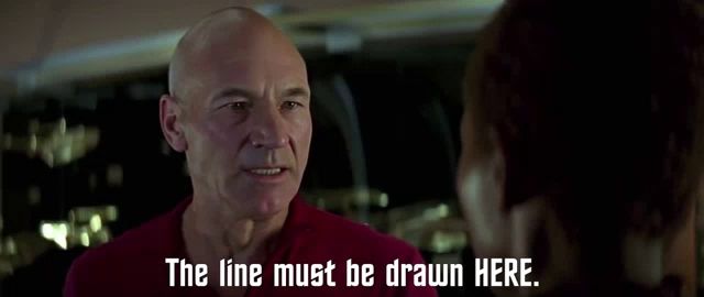 a bald man in a red shirt is talking to a woman with the line must be drawn here