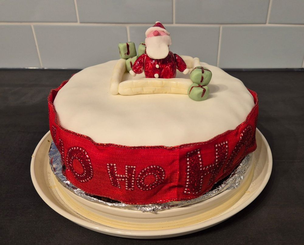 A Christmas cake featuring an icing Father Christmas appearing from a chimney top surrounded by presents