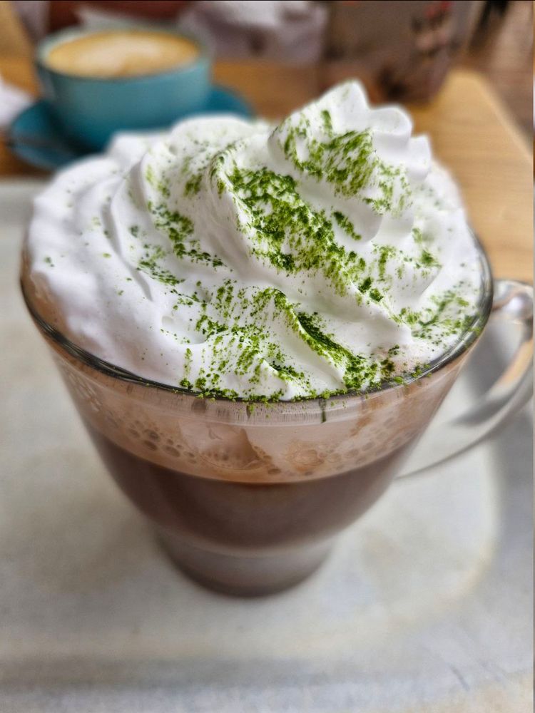 A vegan hot chocolate with vegan cream with matcha on top