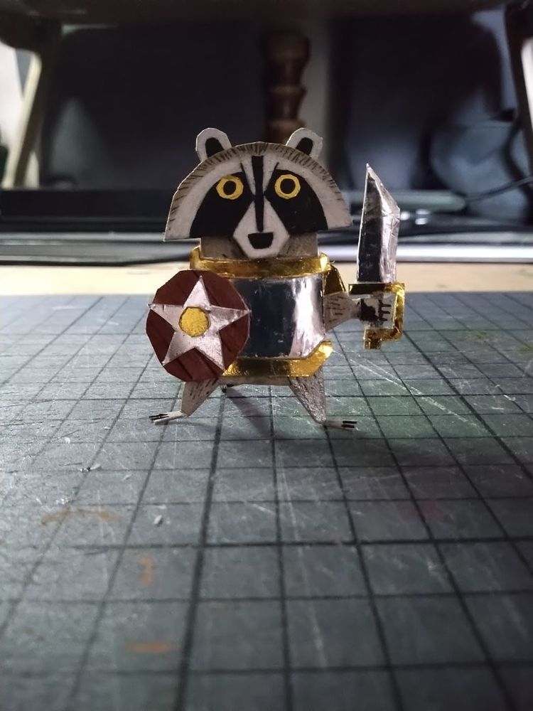 Cut out Raccoon knight with shield and sword. They are wearing silvered paper armour with gold paper detailing
