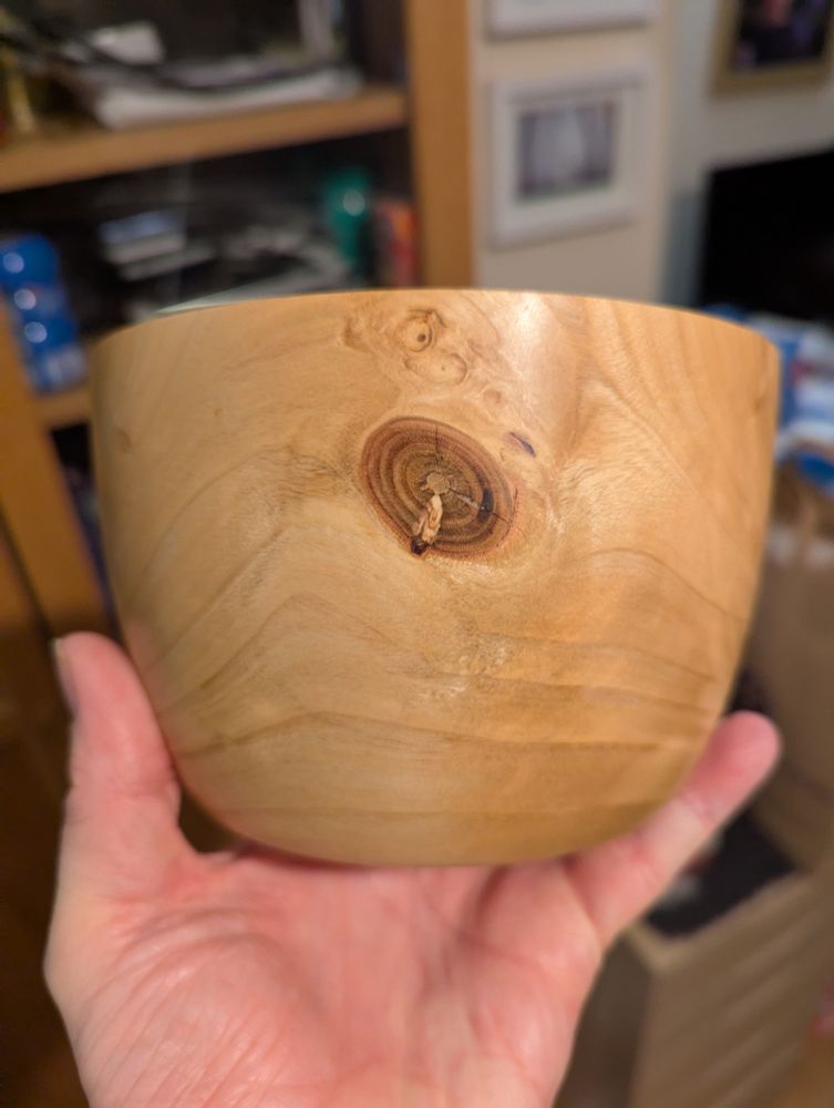 A bowl, turned from cherry, being held in a hand. This shot is the side of the bowl, showing a large knot where a branch had grown out of this trunk.